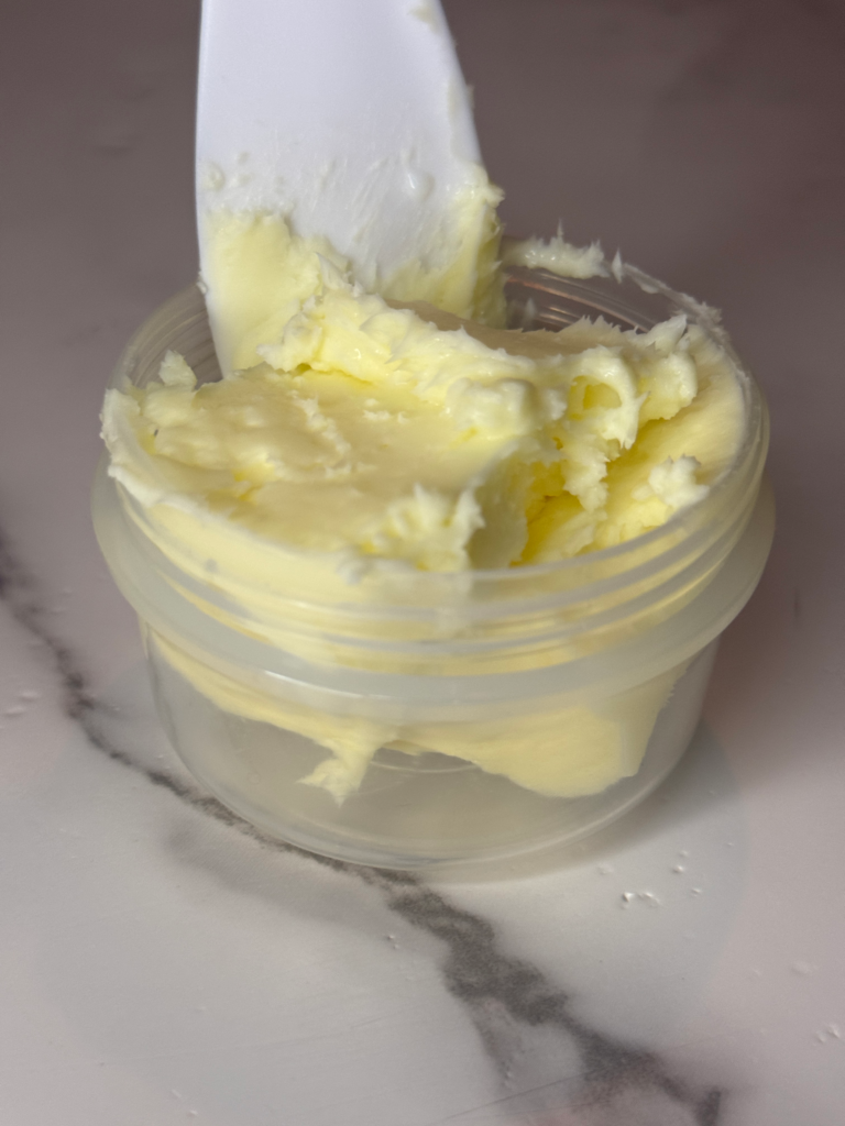 Close-up of creamy homemade butter in a small glass jar with a spatula, showing smooth, freshly whipped texture.