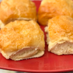 Soft homemade dinner rolls with golden tops on a red plate, showing the fluffy interior after baking.