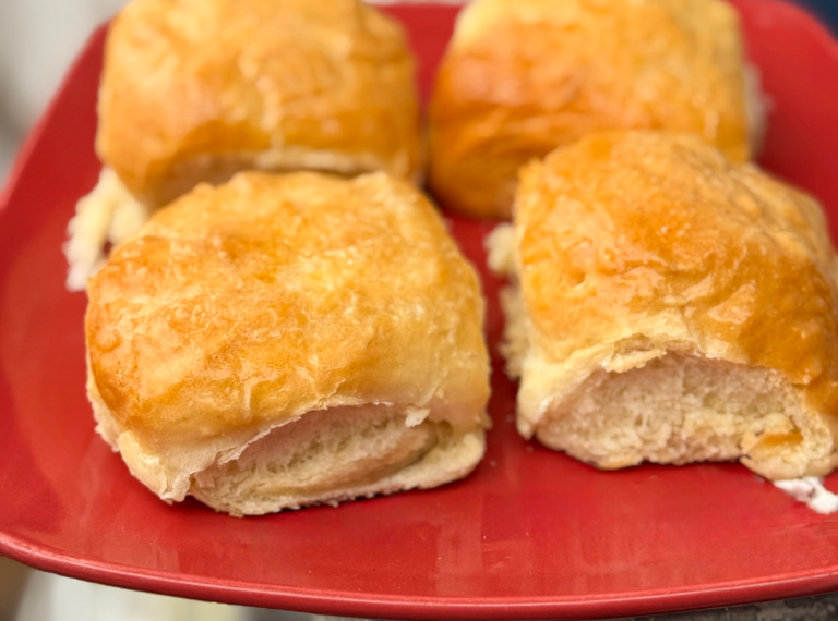 Soft homemade dinner rolls with golden tops on a red plate, showing the fluffy interior after baking.