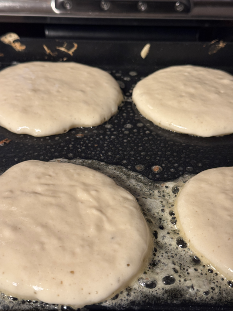 Buttermilk pancake batter cooking on a hot griddle with bubbles forming on top before flipping.