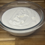Fresh homemade whipped cream in a glass bowl on a wooden surface.