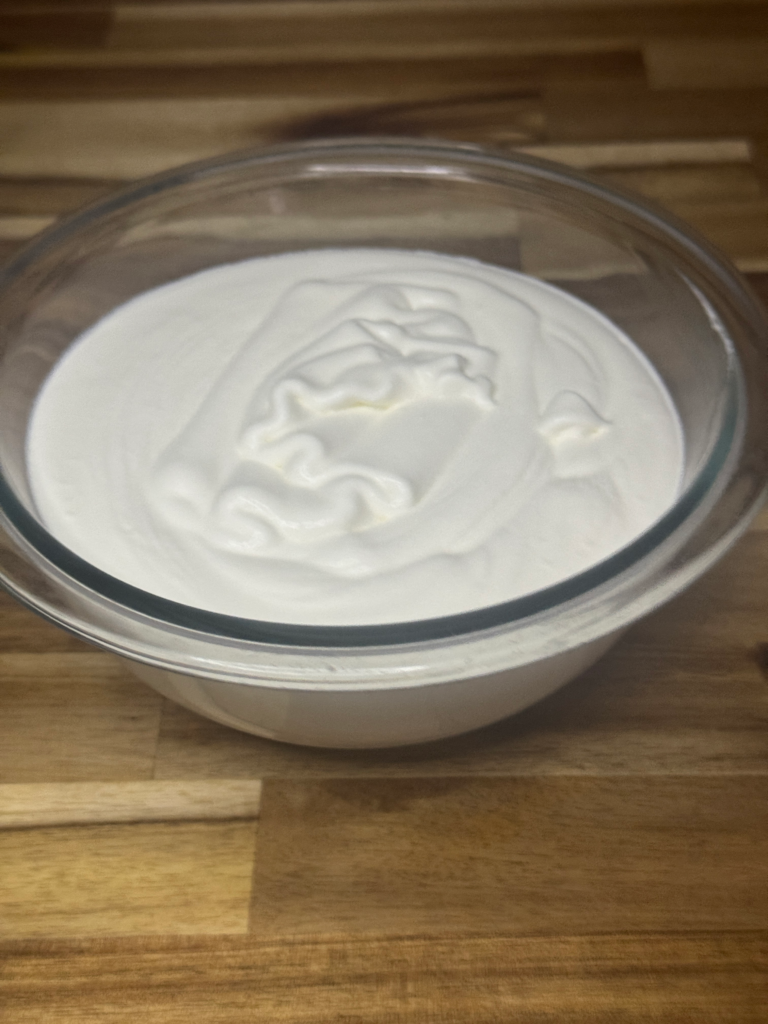 Fresh homemade whipped cream in a glass bowl on a wooden surface.
