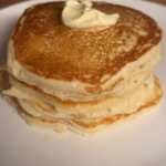 Fluffy golden buttermilk pancakes stacked on a white plate with butter melting on top.
