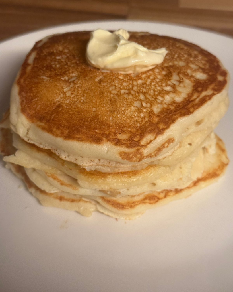 Fluffy golden buttermilk pancakes stacked on a white plate with butter melting on top.