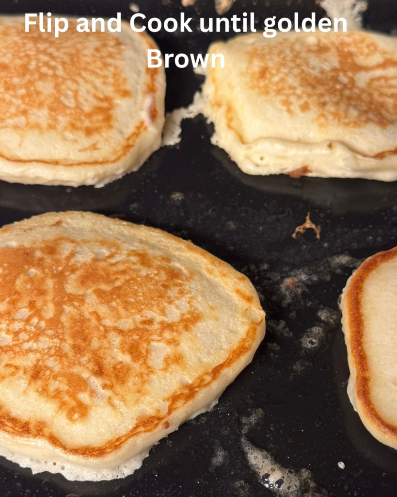 Buttermilk pancakes cooking on a griddle after flipping, golden brown and ready to finish cooking.