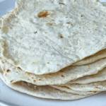 Soft homemade flour tortillas from scratch stacked on a plate for tacos and burritos