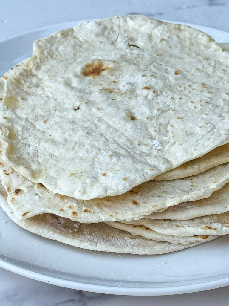 Soft homemade flour tortillas from scratch stacked on a plate for tacos and burritos