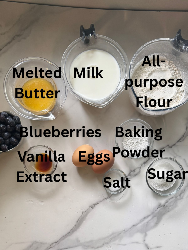 Ingredients for blueberry waffles from scratch including flour, milk, eggs, blueberries, butter, sugar, baking powder, salt, and vanilla extract