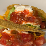 Classic ground beef tacos with shredded cheddar cheese, lettuce, sour cream, and chunky salsa in crispy taco shells.