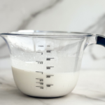 Homemade half and half substitute made with milk and butter in a measuring cup on a marble countertop.