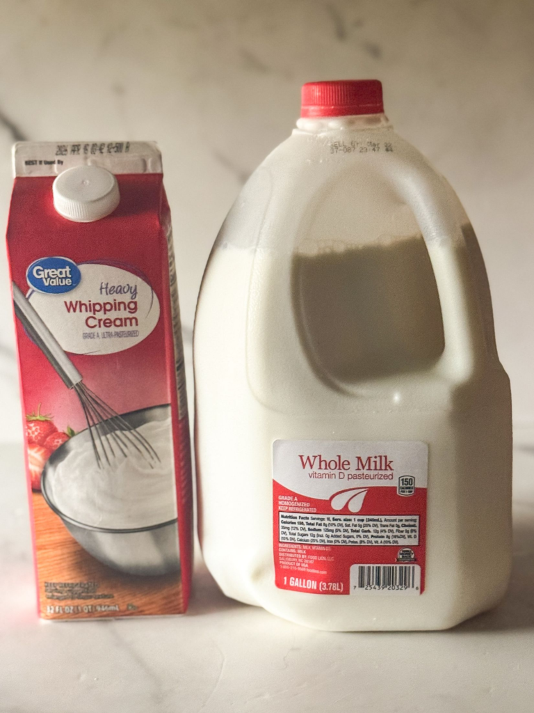 Carton of heavy whipping cream next to a gallon of whole milk on a marble countertop.