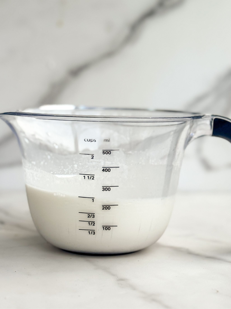 Homemade half and half substitute made with milk and butter in a measuring cup on a marble countertop.