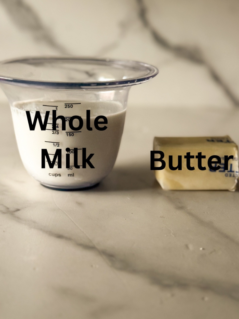 Milk in a measuring cup with butter on a marble countertop for making a homemade heavy cream substitute.