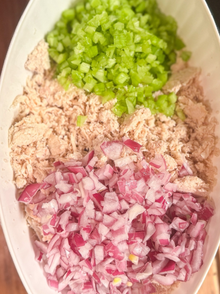 Shredded chicken with diced celery and red onion in a bowl ready to make chicken salad