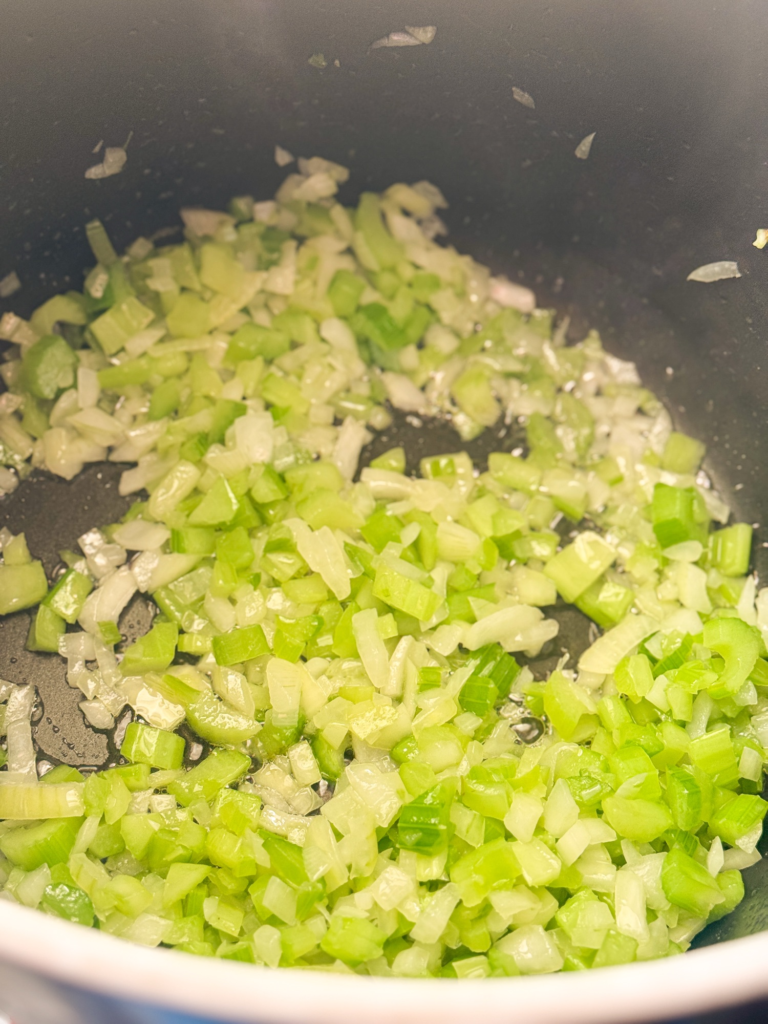 Diced celery and onion sautéing in a pot as the first step for making homemade chicken and dumplings from scratch.