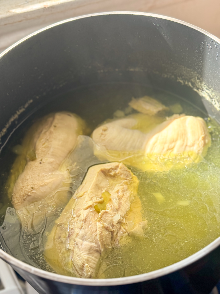 Chicken breasts simmering in broth with onions and celery for homemade chicken and dumplings