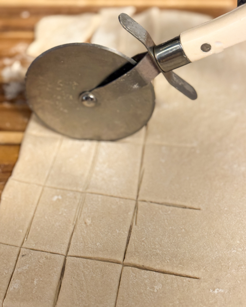 Cutting rolled dumpling dough into squares with a pizza cutter for homemade chicken and dumplings.