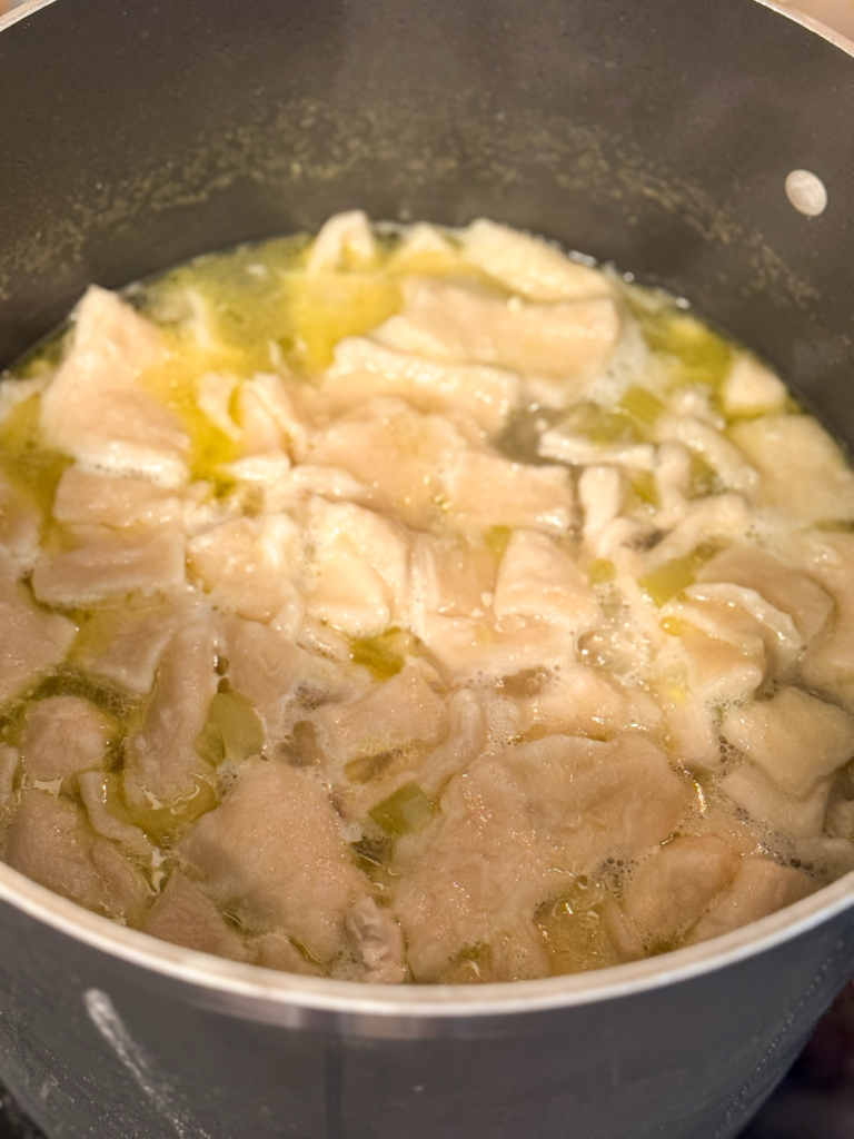 Homemade dumplings simmering in broth while making chicken and dumplings from scratch.
