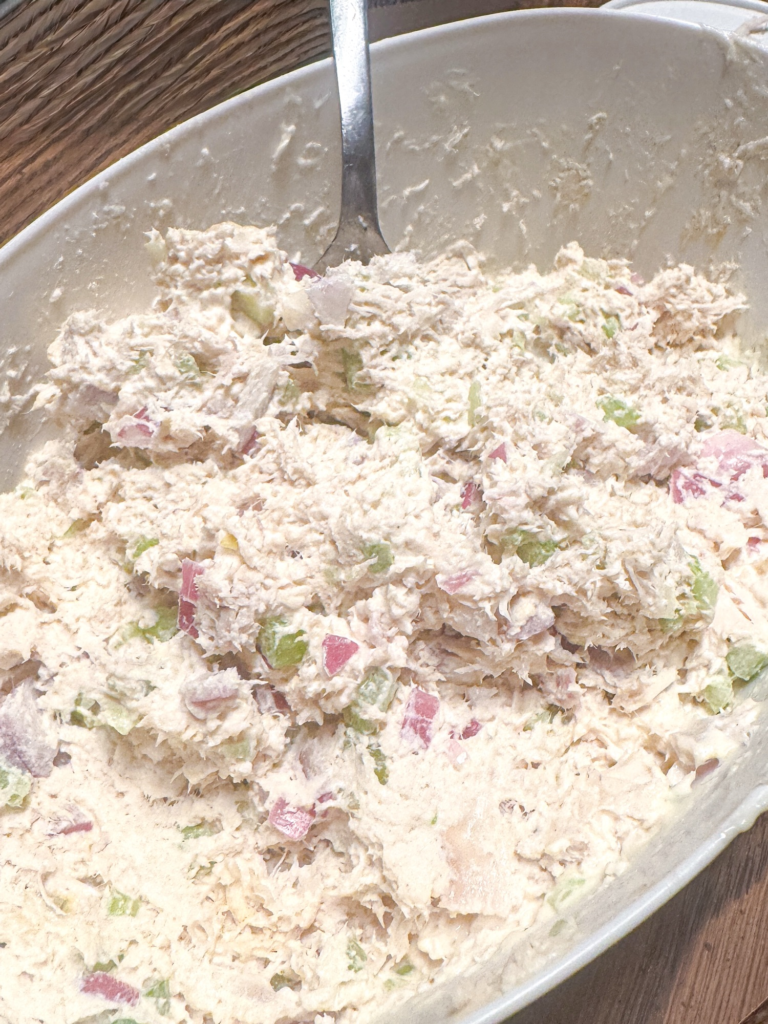 Creamy chicken salad mixed together with shredded chicken, celery, and red onion in a bowl