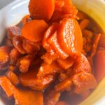 Spoon lifting southern candied sweet potatoes coated in a rich brown sugar glaze in a white bowl