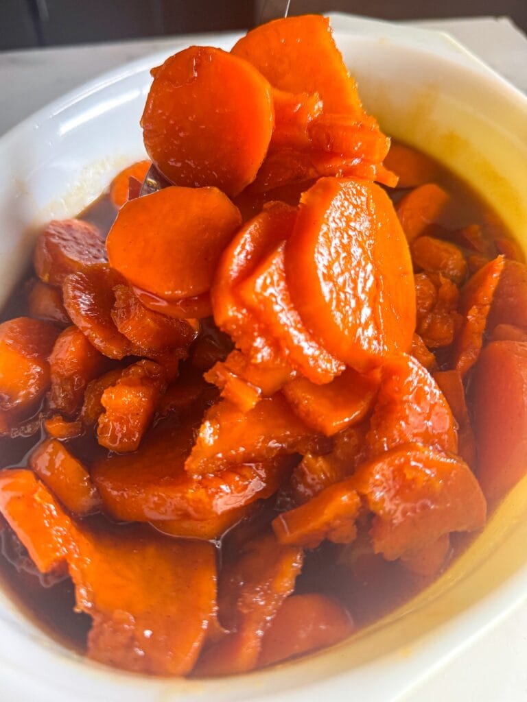Spoon lifting southern candied sweet potatoes coated in a rich brown sugar glaze in a white bowl