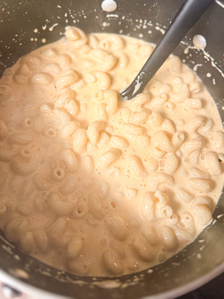 Cooked pasta being stirred into creamy cheese sauce in a pot for Tini’s viral TikTok baked mac and cheese recipe
