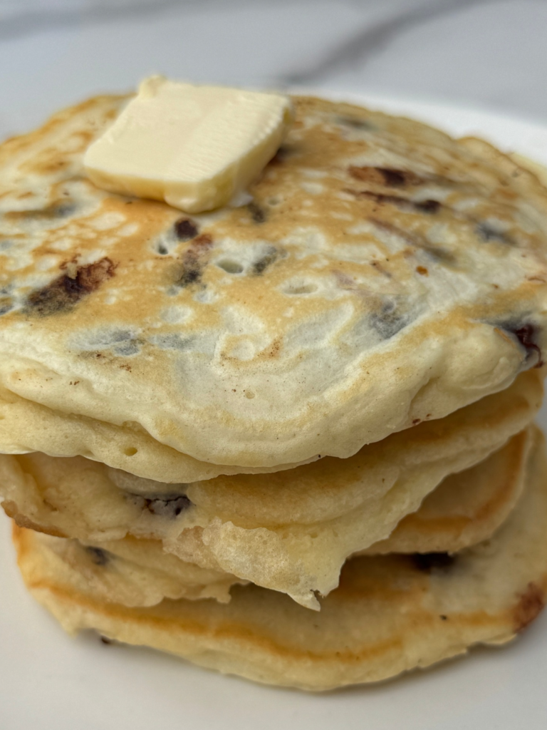 Stack of easy chocolate chip pancakes from scratch topped with butter and syrup on a white plate.