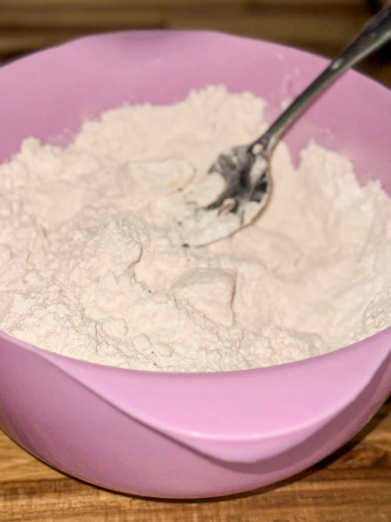 Flour and baking ingredients being mixed together in a pink bowl with a spoon to make homemade Bisquick mix