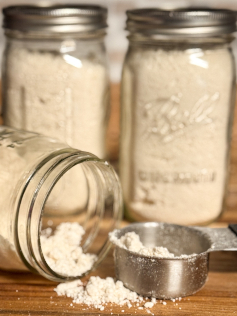 Homemade Bisquick mix stored in mason jars with a measuring cup on a wooden countertop
