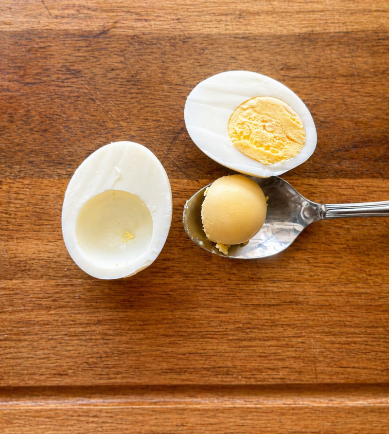 Removing Egg Yolks for Deviled Eggs Cut hard-boiled egg with yolk being removed for deviled eggs recipe