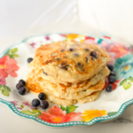 Easy blueberry pancakes from scratch stacked on a floral plate with fresh blueberries on the side.