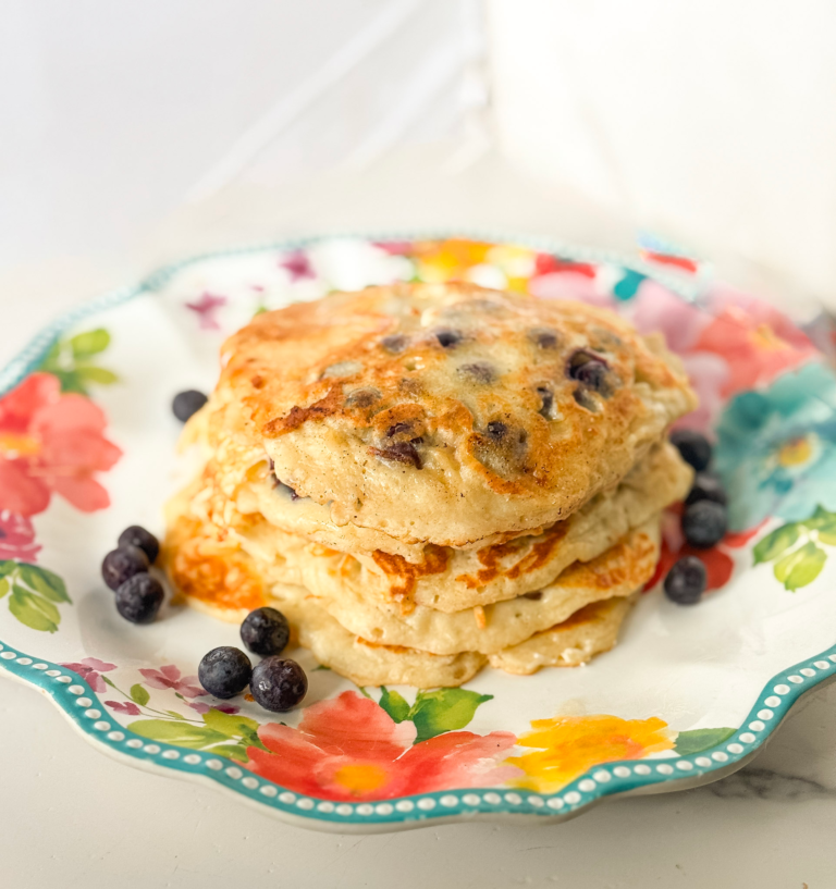 Easy blueberry pancakes from scratch stacked on a floral plate with fresh blueberries on the side.