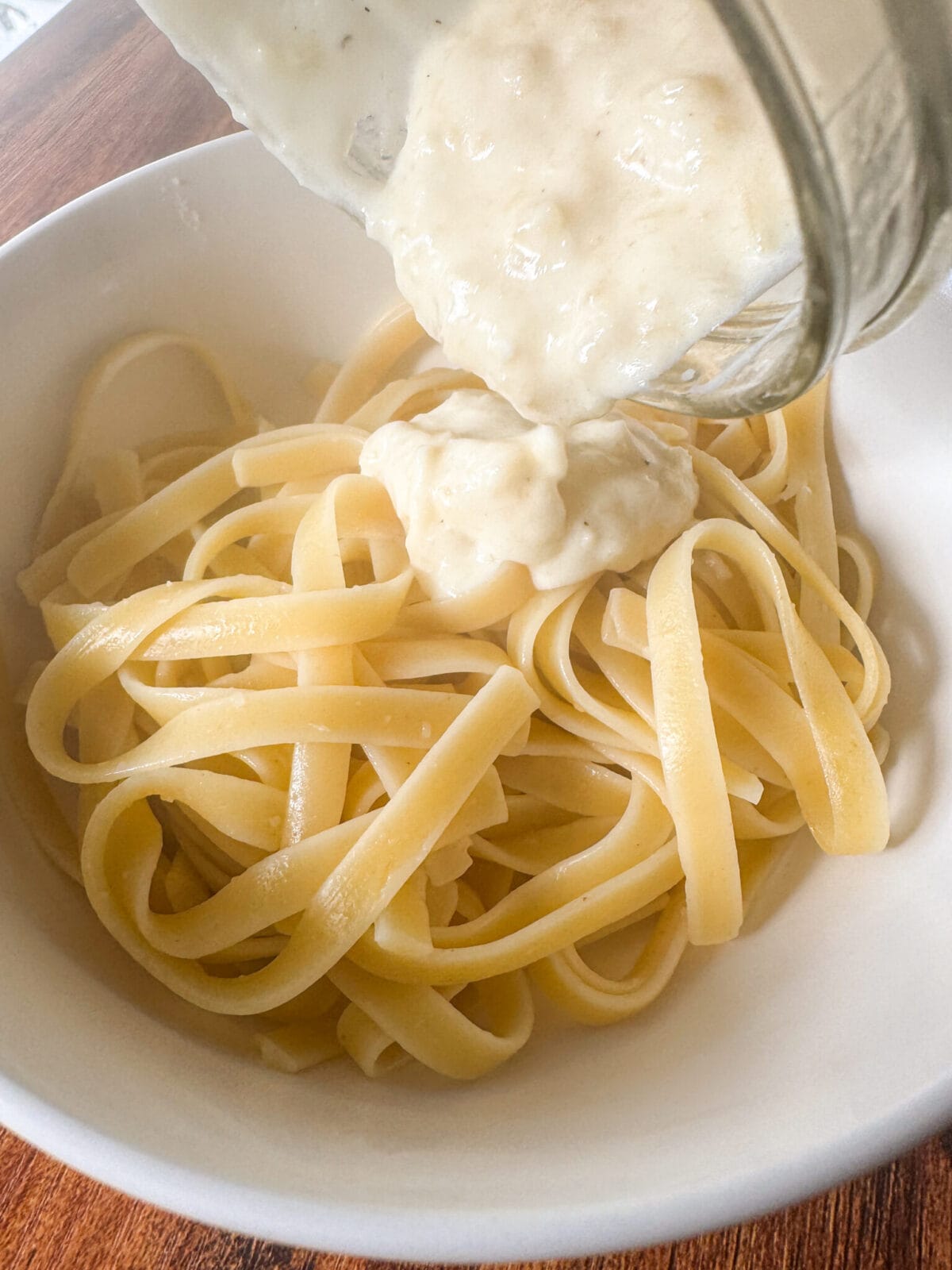 Easy homemade Alfredo sauce being poured over fettuccine pasta in a white bowl