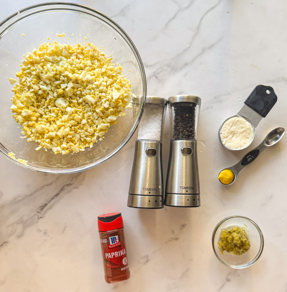 ingredients for egg salad including chopped eggs, mayonnaise, mustard, relish, salt, pepper, and paprika
