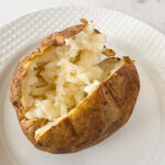 Fluffy baked potato with crispy skin split open on a white plate