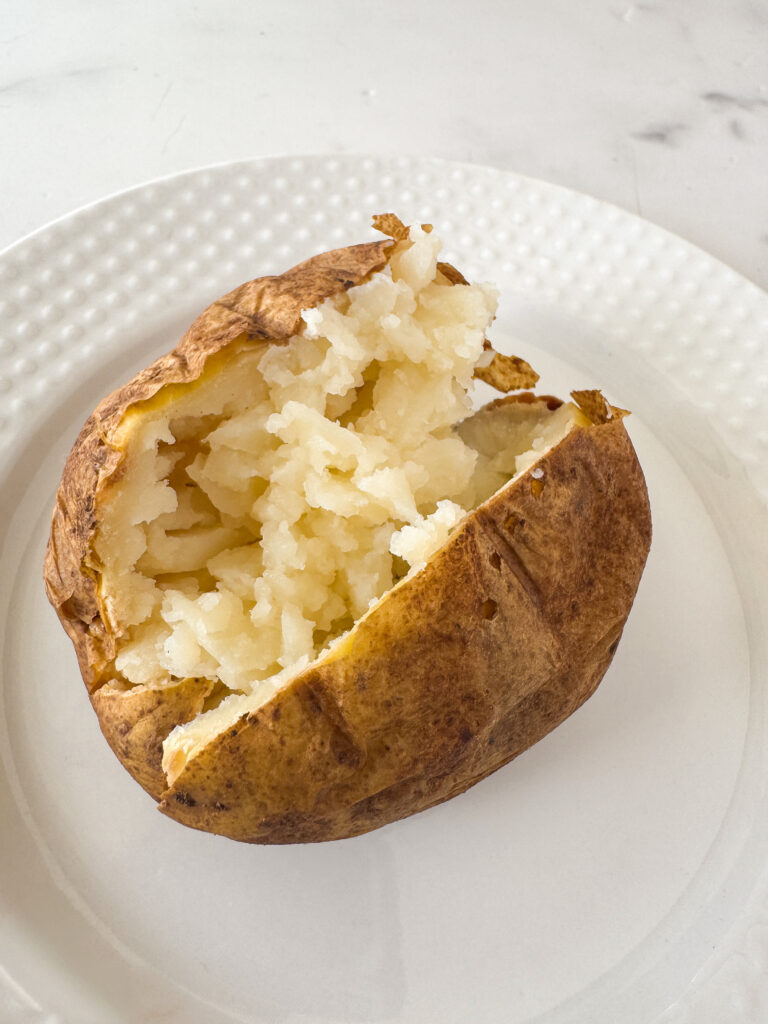 Fluffy baked potato with crispy skin split open on a white plate