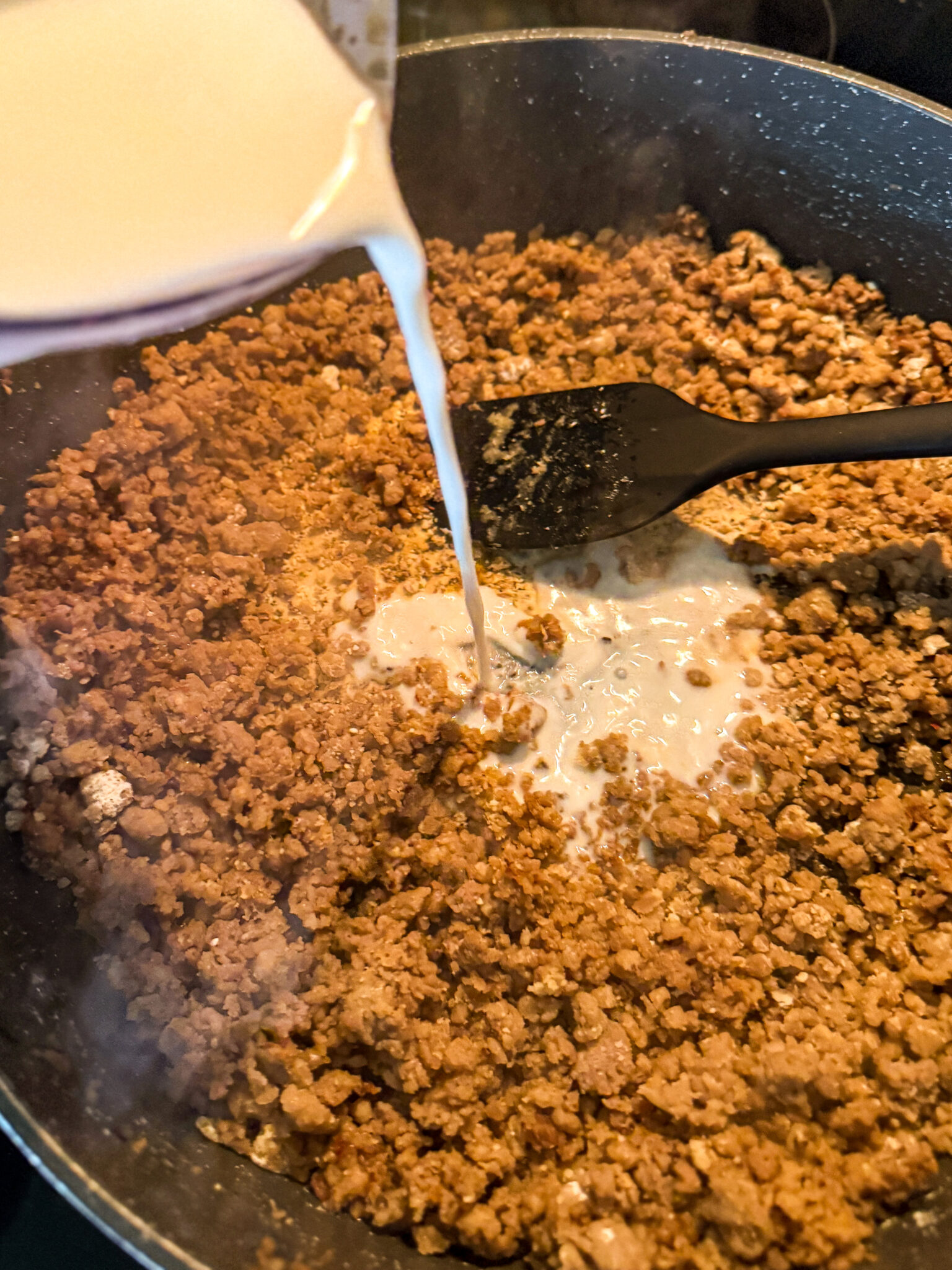 Adding Milk to Sausage Gravy pouring milk into sausage and flour mixture to make homemade sausage gravy